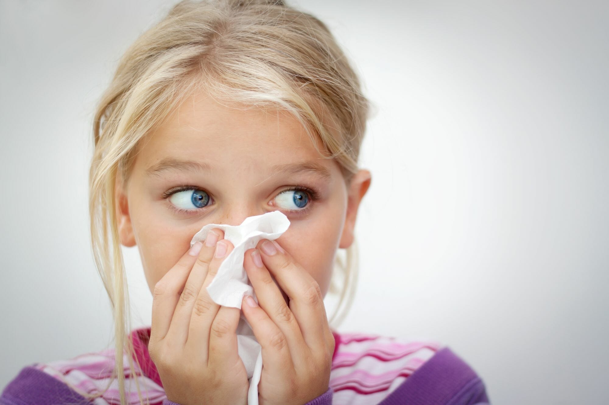 A little girl blowing her nose with a tissue at a pediatrician's office in Sugar Land.