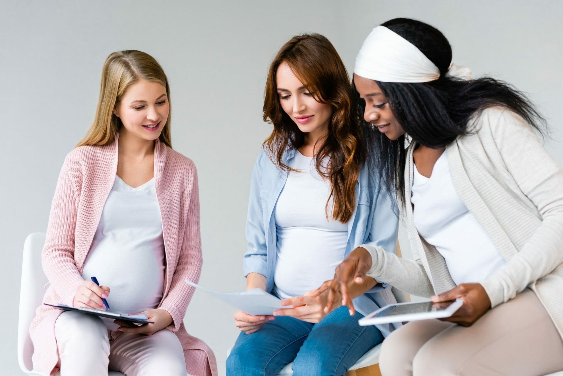 Three pregnant women sitting on a chair with their tablets.