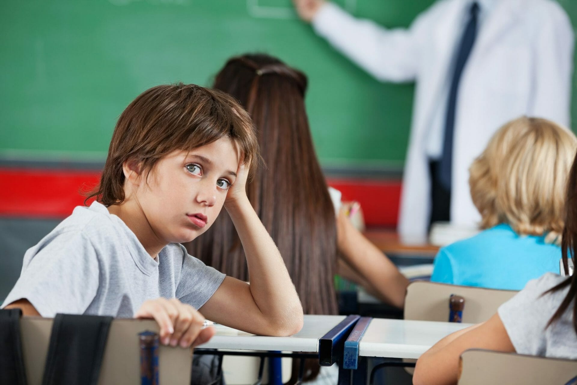 A boy is sitting at a desk in front of a blackboard in Sugar Land.